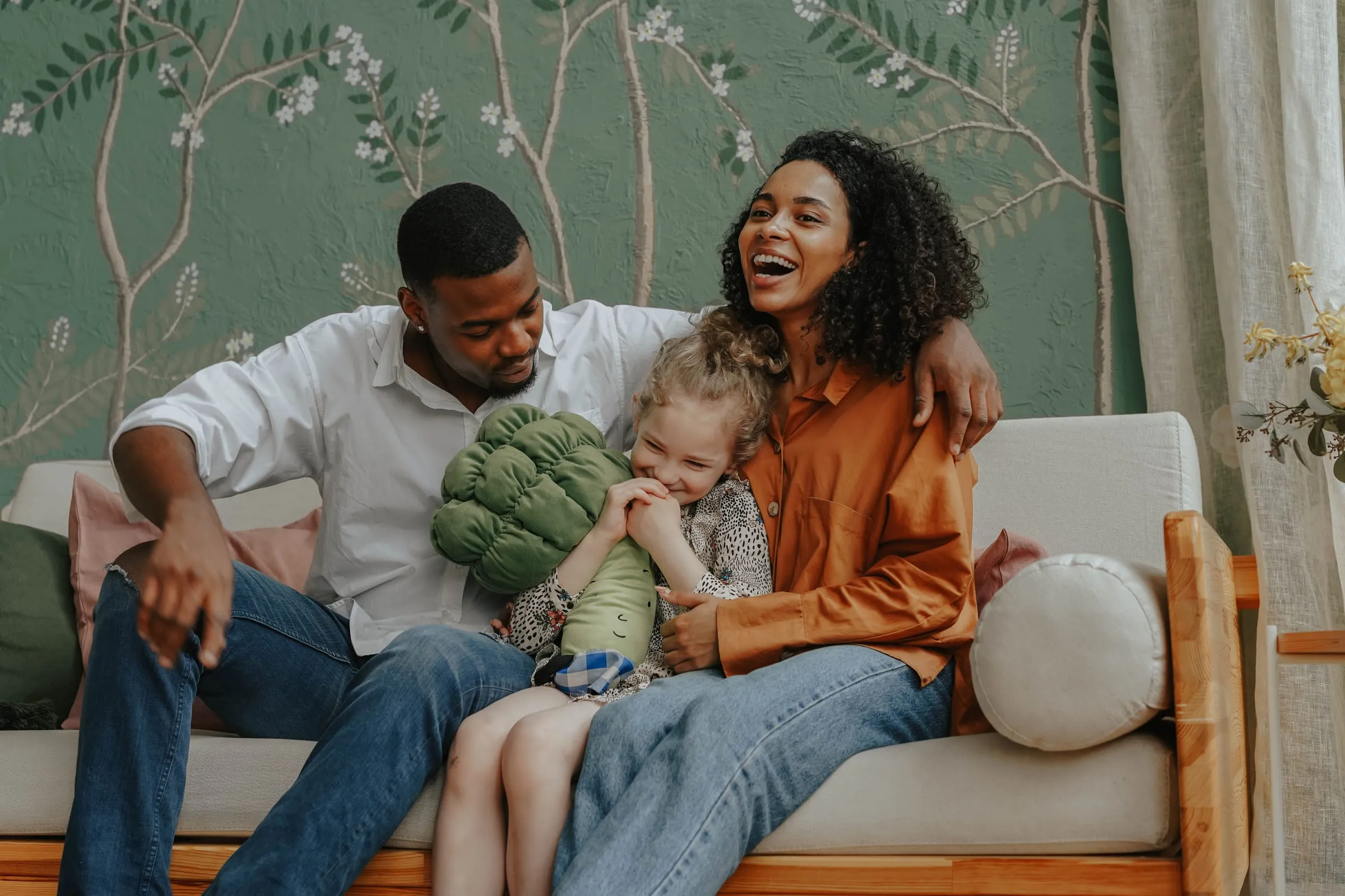 A laughing family of three on their living room couch