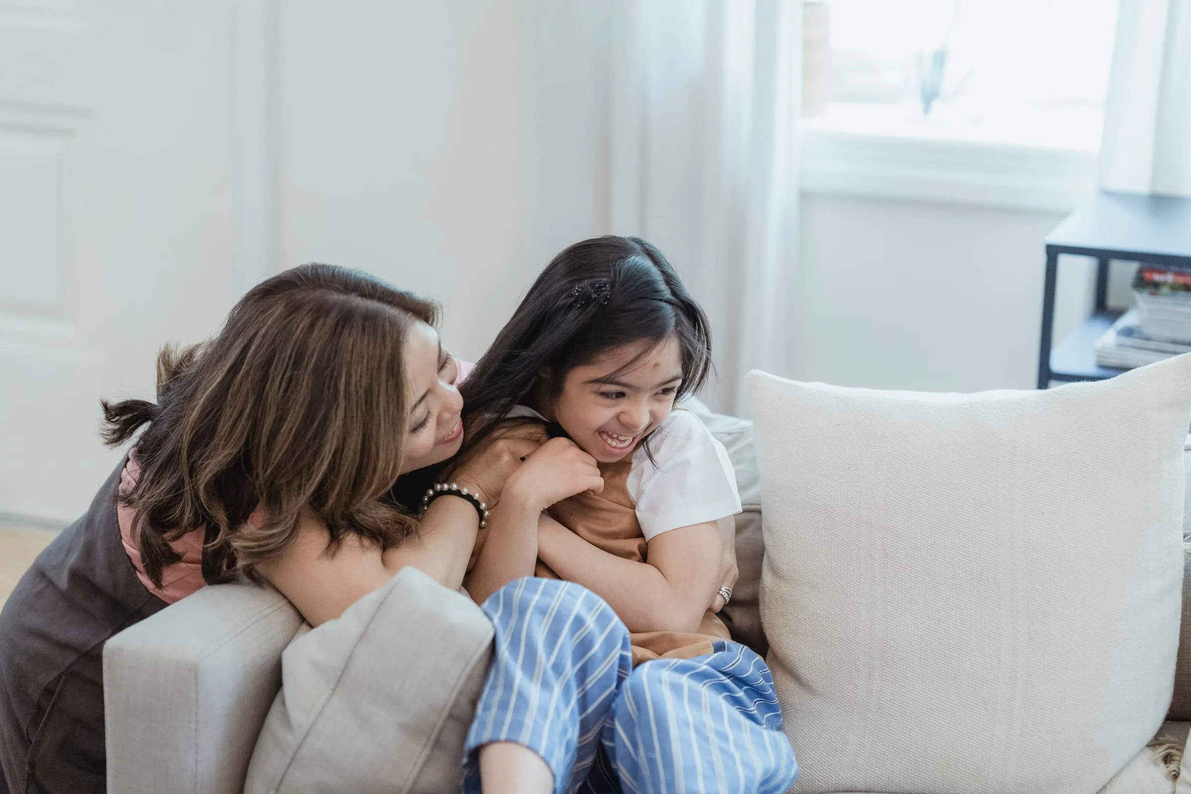 A mother and daughter hugging and laughing on the couch