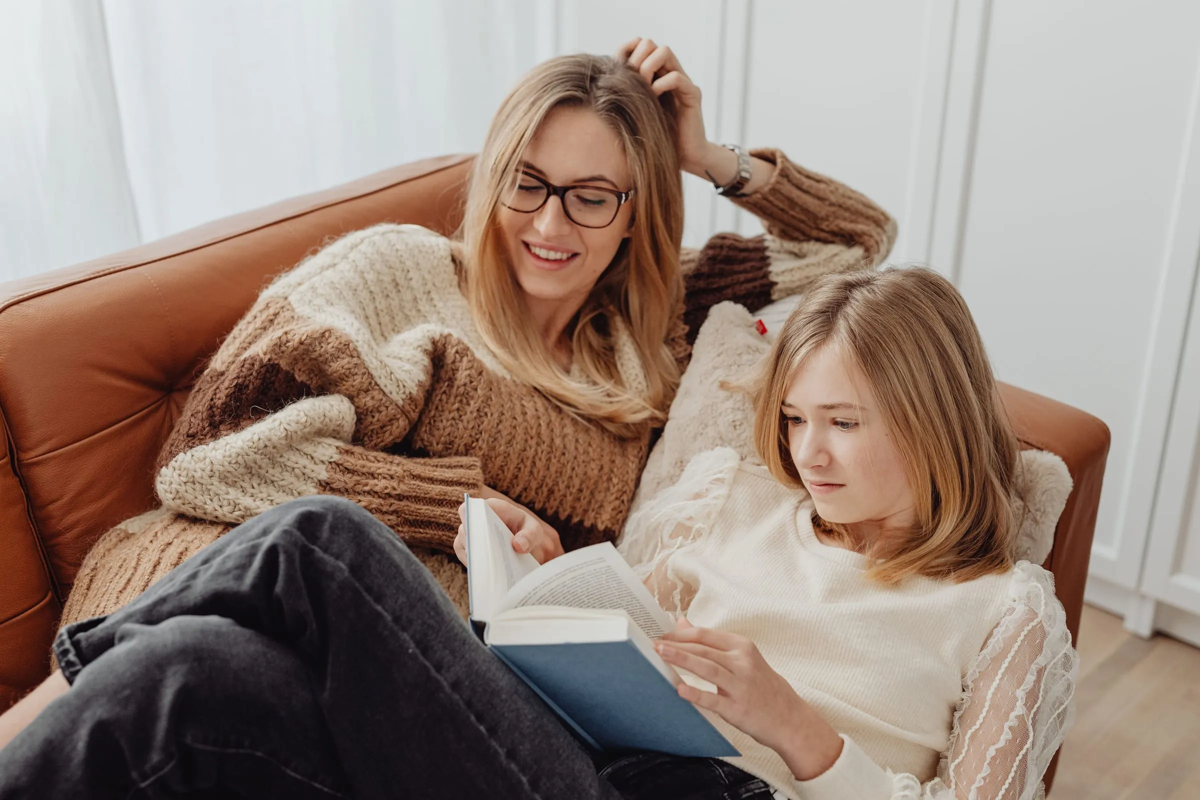 A mother and her teenage daughter reading together on the couch